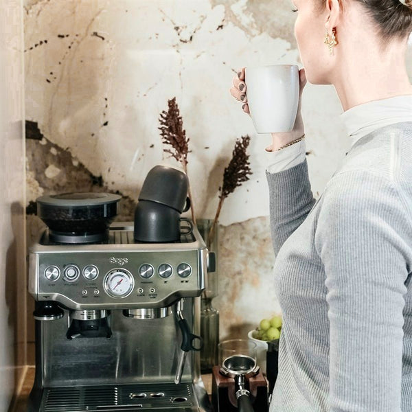 En kvinde drikker kaffe ved sin espressomaskine