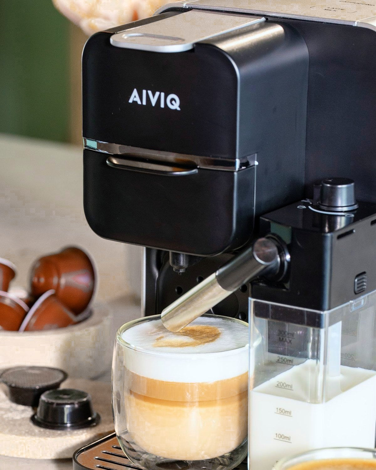 AIVIQ MultiBrew Pro med en latte, kapsler og mælkebeholderen på et stenbord