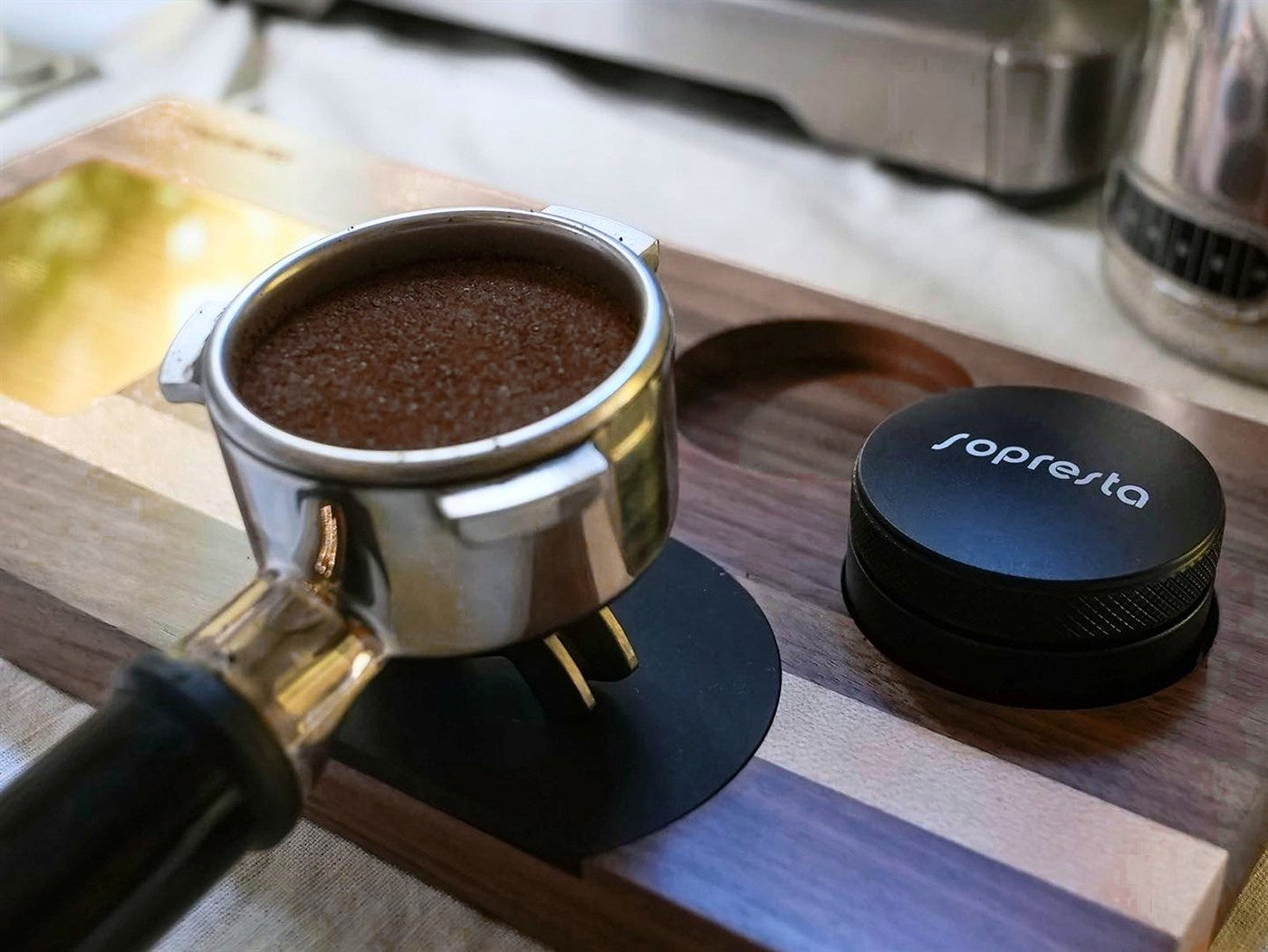 Et portafilter med kaffe i en Sopresta-station i valnød ved siden af en kaffefordeler