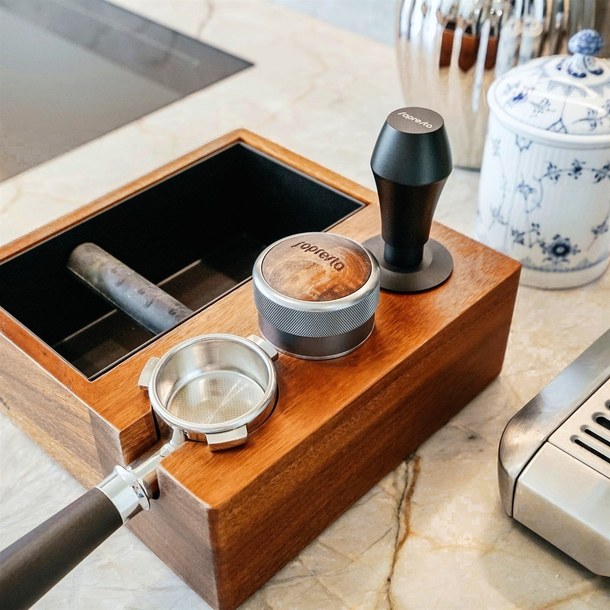 Sopresta Premium-tamperstation med knockbox i valnød med tamper, fordeler og portafilter på et marmorbord