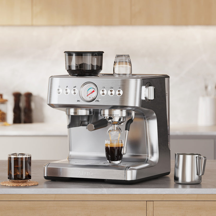 Espressomaskine i børstet stål på en grå stenbordplade, hvor espresso løber ned i et lille glas, med en glaskrukke med kaffebønner til venstre og en mælkekande i stål til højre