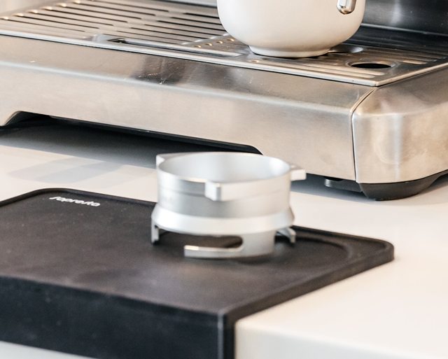 Sopresta kaffekværn-tragt på en tampermåtte foran en espressomaskine